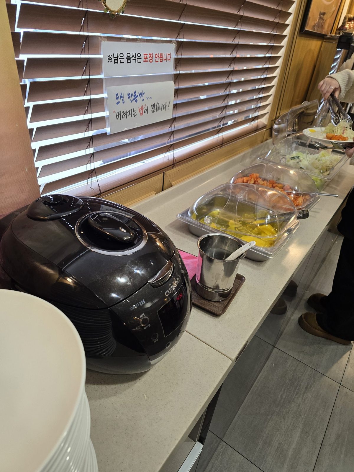 Self-service banchan bar with rice cooker, pickled radish, kimchi, and coleslaw