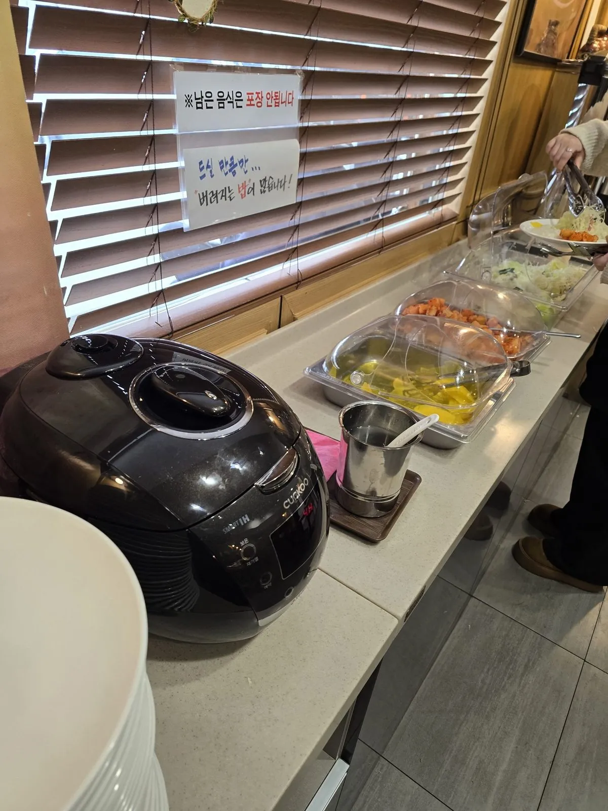 Self-service banchan bar with rice cooker, pickled radish, kimchi, and coleslaw
