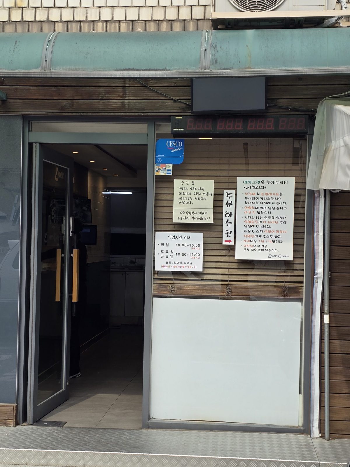 The entrance with handwritten signs showing business hours and ordering instructions